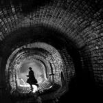 Zwart-witbeeld van een silhouet in een donkere bakstenen tunnel