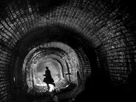 Zwart-witbeeld van een silhouet in een donkere bakstenen tunnel